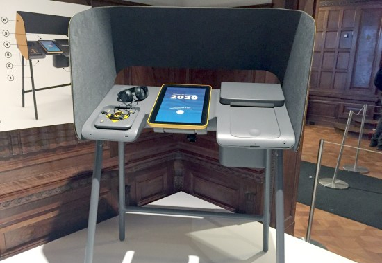 Accessible voting booth with headphones and tablet computer display as well as tactile input module. Booth and devices have rounded co