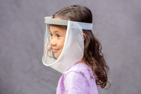 A young girl wears a face shield with a cloth mane attached to its perimeter.